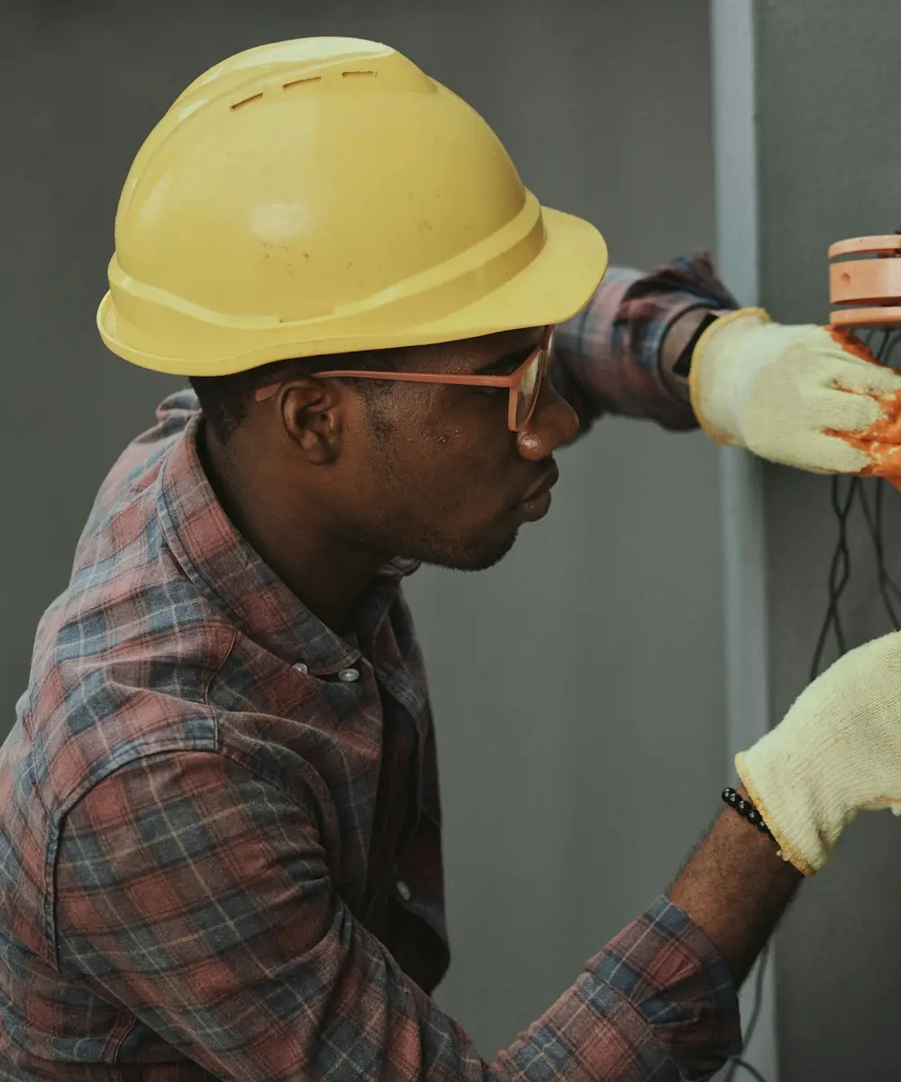 Technician in a hard hat and work gloves servicing heating equipment on a basement wall